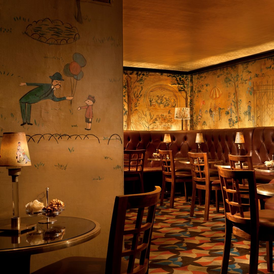 A dining area with green chairs, artwork, a fireplace, and elegantly set tables.